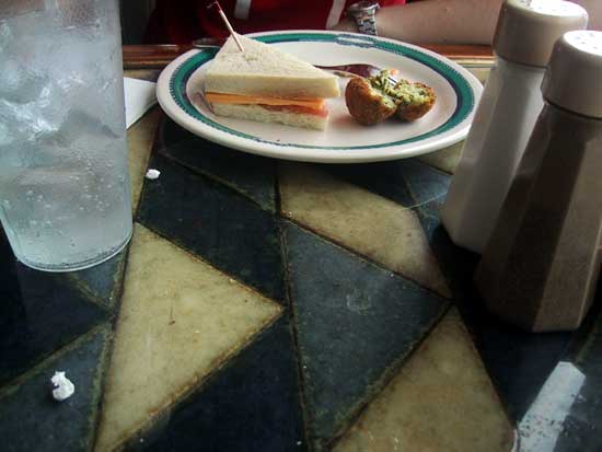 [ a sandwich sits between salt and pepper shakers on the right and a glass of ice water on the left ]